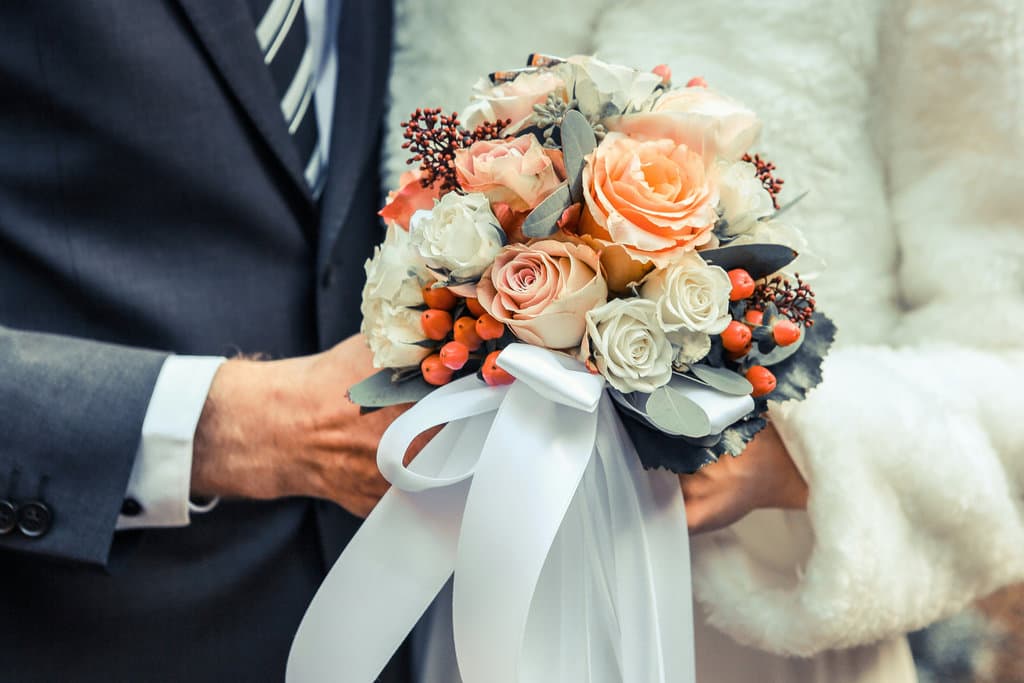 The bridal bouquet in the hands of the bride and groom.